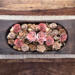 Large rustic wood dough bowl centerpiece on coffee table. Filled with natural botanicals and flower blossoms in pink and taupe.